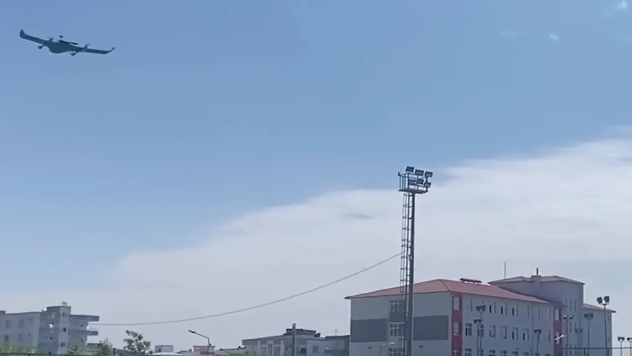 CEZERİ ROBOTECH takımının ürettiği yeşil sabit kanatlı İHA'nın okul sahası üzerindeki uçuş gösterisi ve izleyen öğrenciler